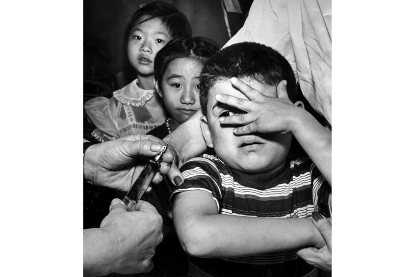 Feb. 25, 1957: Manuel Reyes, 7, peeks apprehensively between fingers at needle just before getting his polio shot at Castelar Street School as two little girls await their turn. Yesterday the city opened drive to immunize 300,000 children. Photo by Garry Watson/Los Angeles Times