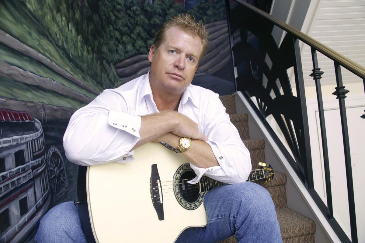 A man sits on a staircase with his arms resting atop an acoustic guitar 