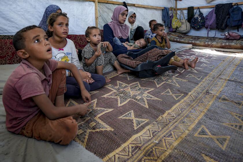 CAPTION CORRECTION: Displaced infant Abdel-Rahman Abu El-Jedian, 11-month-old, who suffers from polio, is carried by his mother, center, at a makeshift tent camp in Deir al-Balah, central Gaza Strip, Tuesday, Aug. 27, 2024. (AP Photo/Abdel Kareem Hana)