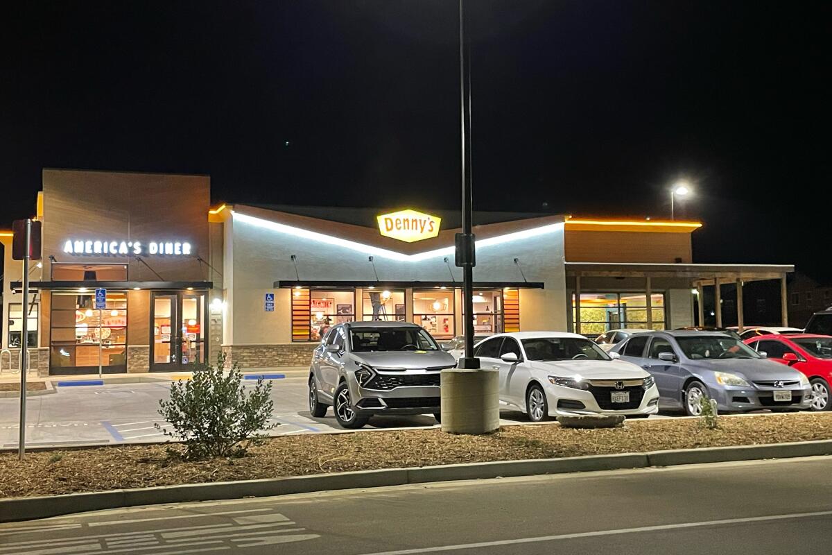 Cars parked in front of a diner with a sign that says Denny's under dark skies