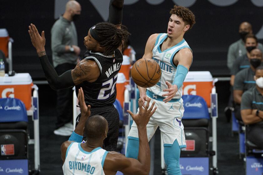 Charlotte Hornets guard LaMelo Ball (2) passes the ball around Sacramento Kings center Richaun Holmes (22) to teammate Bismack Biyombo during the first quarter of an NBA basketball game in Sacramento, Calif., Sunday, Feb. 28, 2021. (AP Photo/Randall Benton)