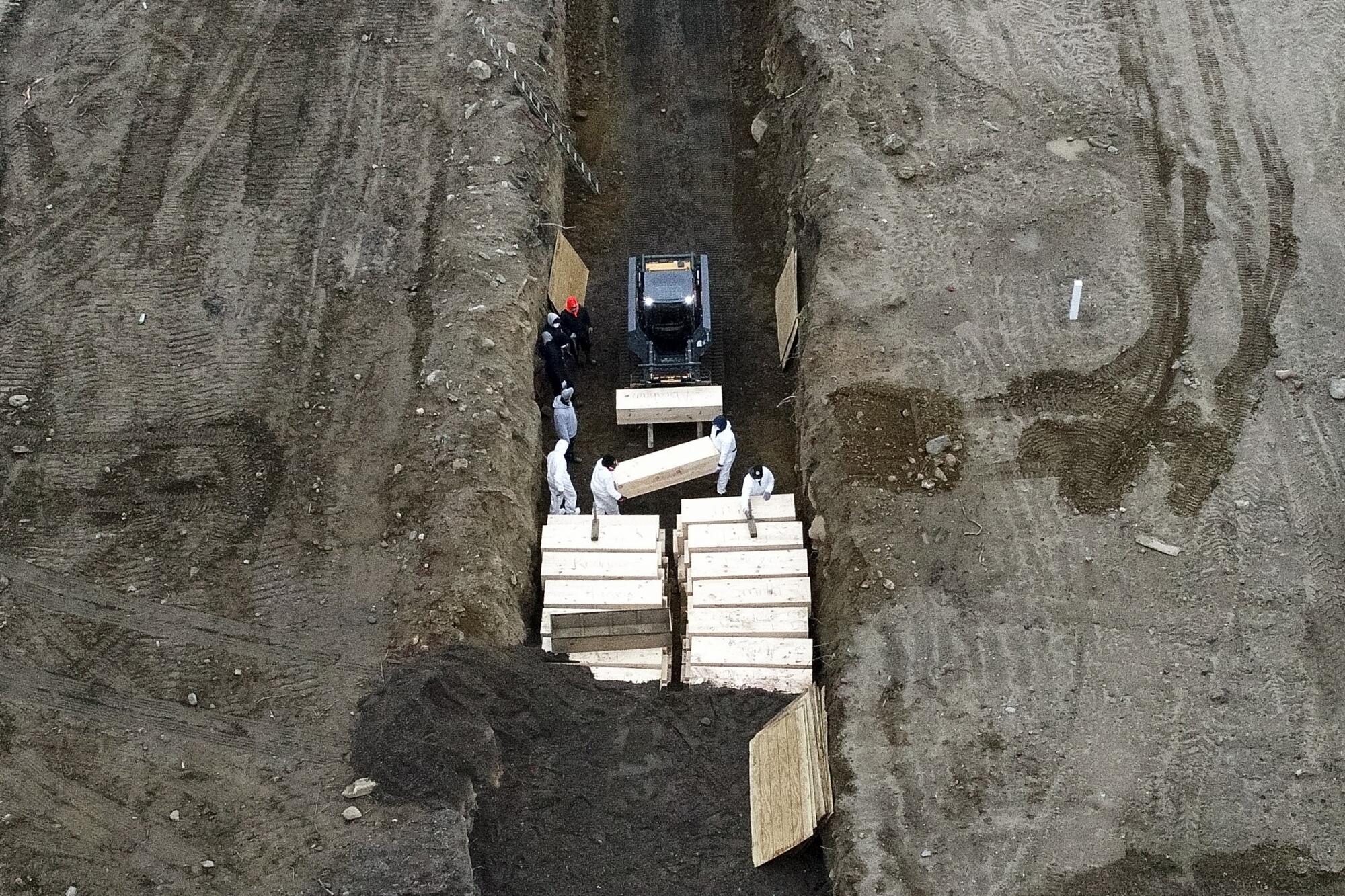 Workers wearing personal protective equipment bury bodies April 9 in a trench on Hart Island in the Bronx, N.Y.