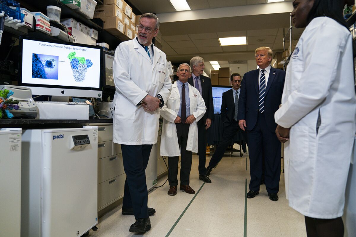 President Trump stands amid doctors in white coats in a lab.