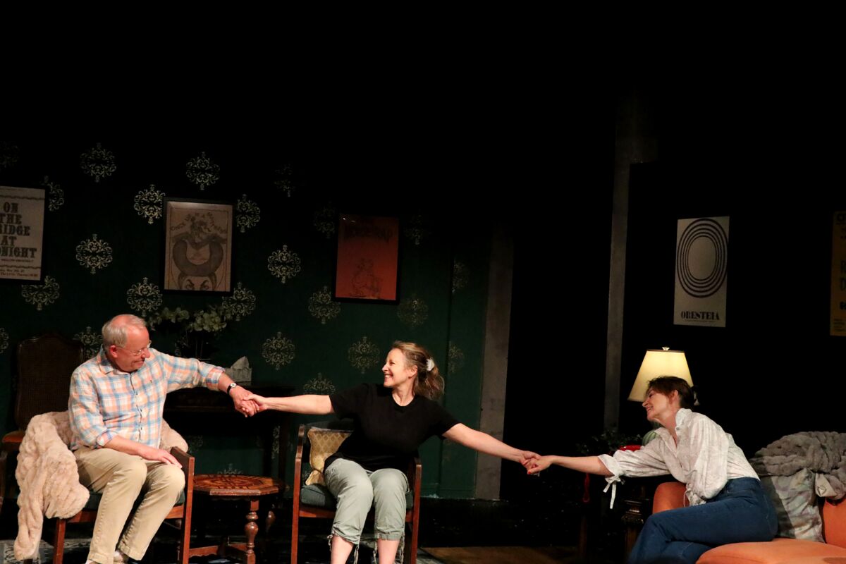 Three seated actors link hands.
