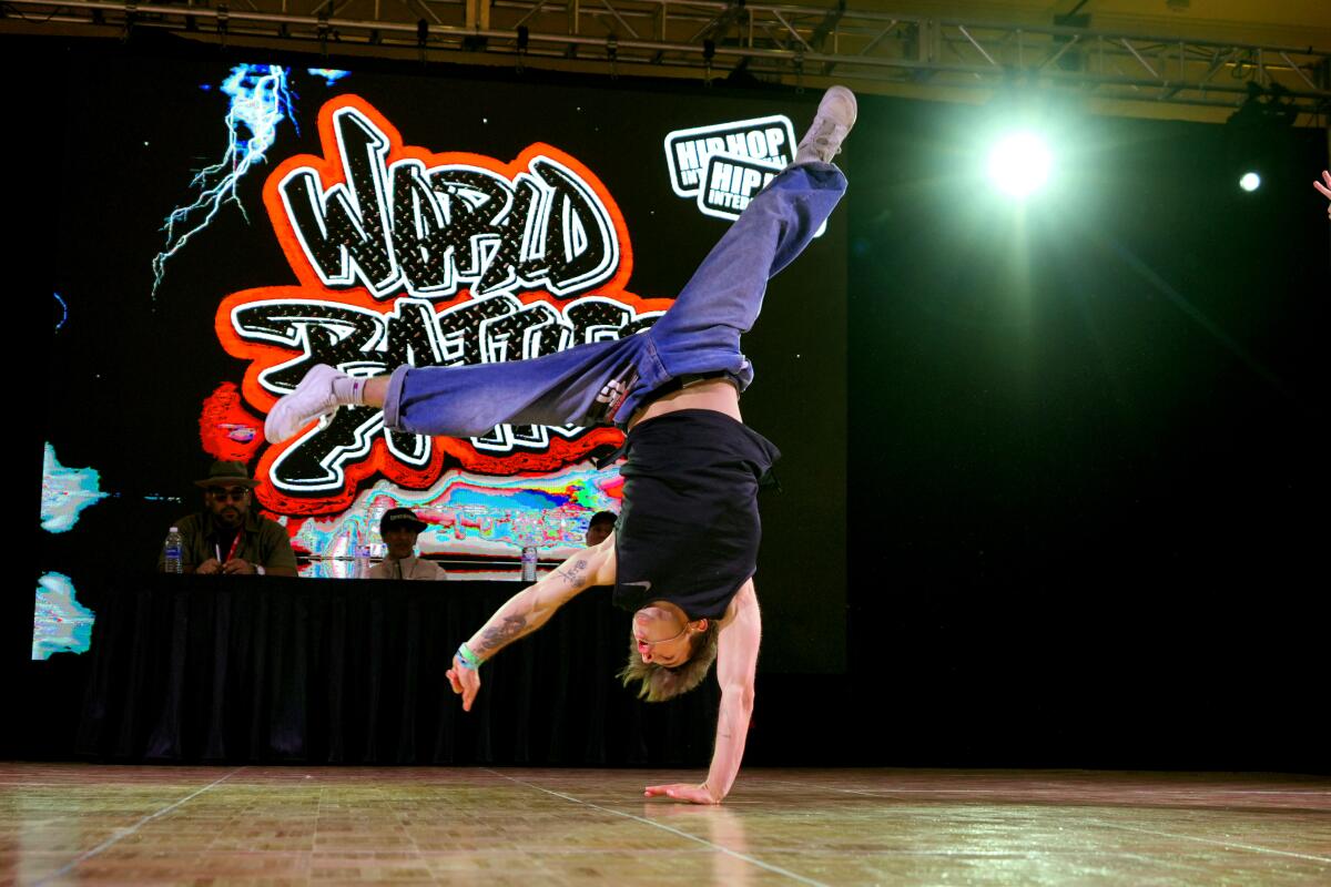 A hip-hop dancer does a handstand while competing on stage.