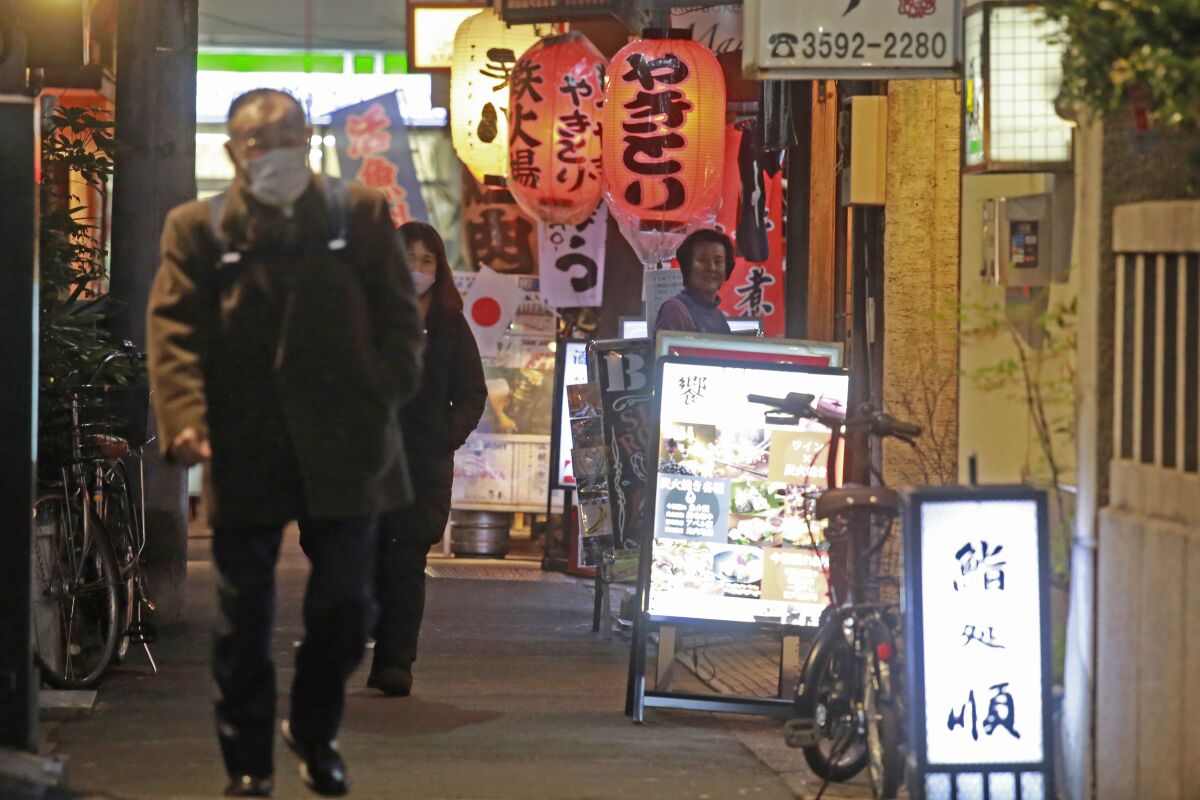 People wearing face masks to help protect against the spread of the coronavirus walk on a street lined with bars and restaurants in Tokyo Wednesday, Jan. 19, 2022. Tokyo and a dozen other areas in Japan are set to face new COVID-19 restrictions effective Friday, with local leaders shortening hours for restaurants, as omicron cases hit a record high in the capital. (AP Photo/Koji Sasahara)