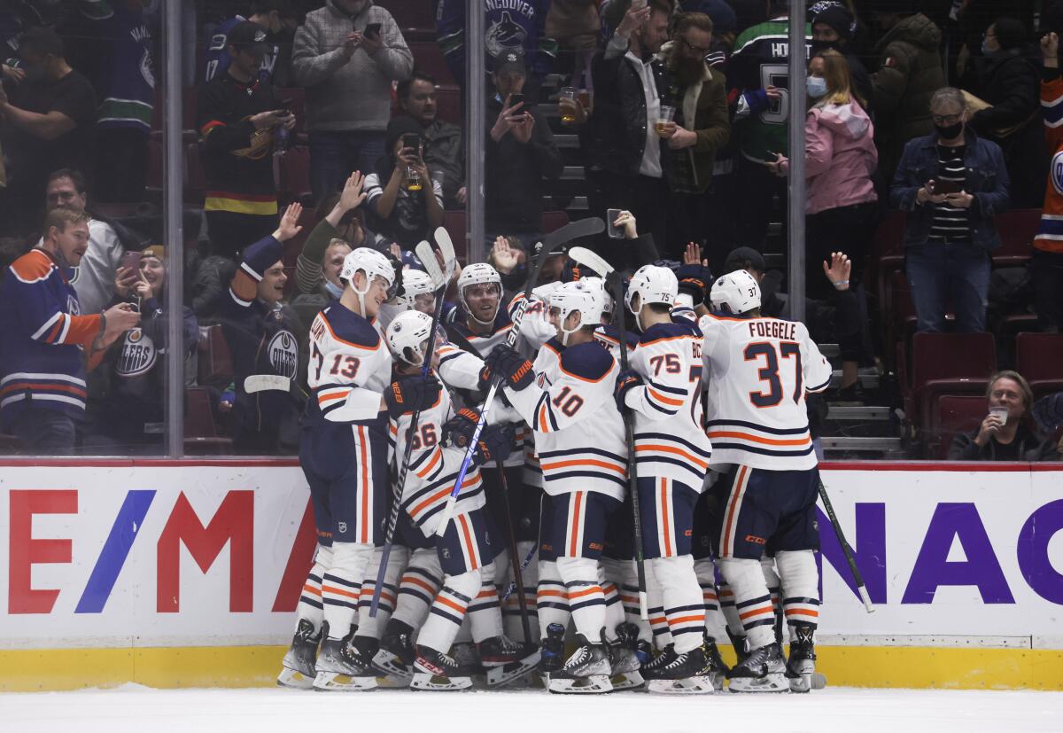 Edmonton Oilers' Connor McDavid, back center, is mobbed by his teammates after scoring the winning goal during overtime in an NHL hockey game, Tuesday, Jan. 25, 2022 in Vancouver, British Columbia. (Darryl Dyck/The Canadian Press via AP)