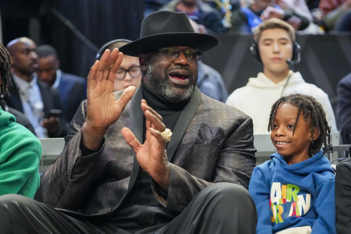 Shaquille O'Neal, wearing a hat, watches a basketball game.