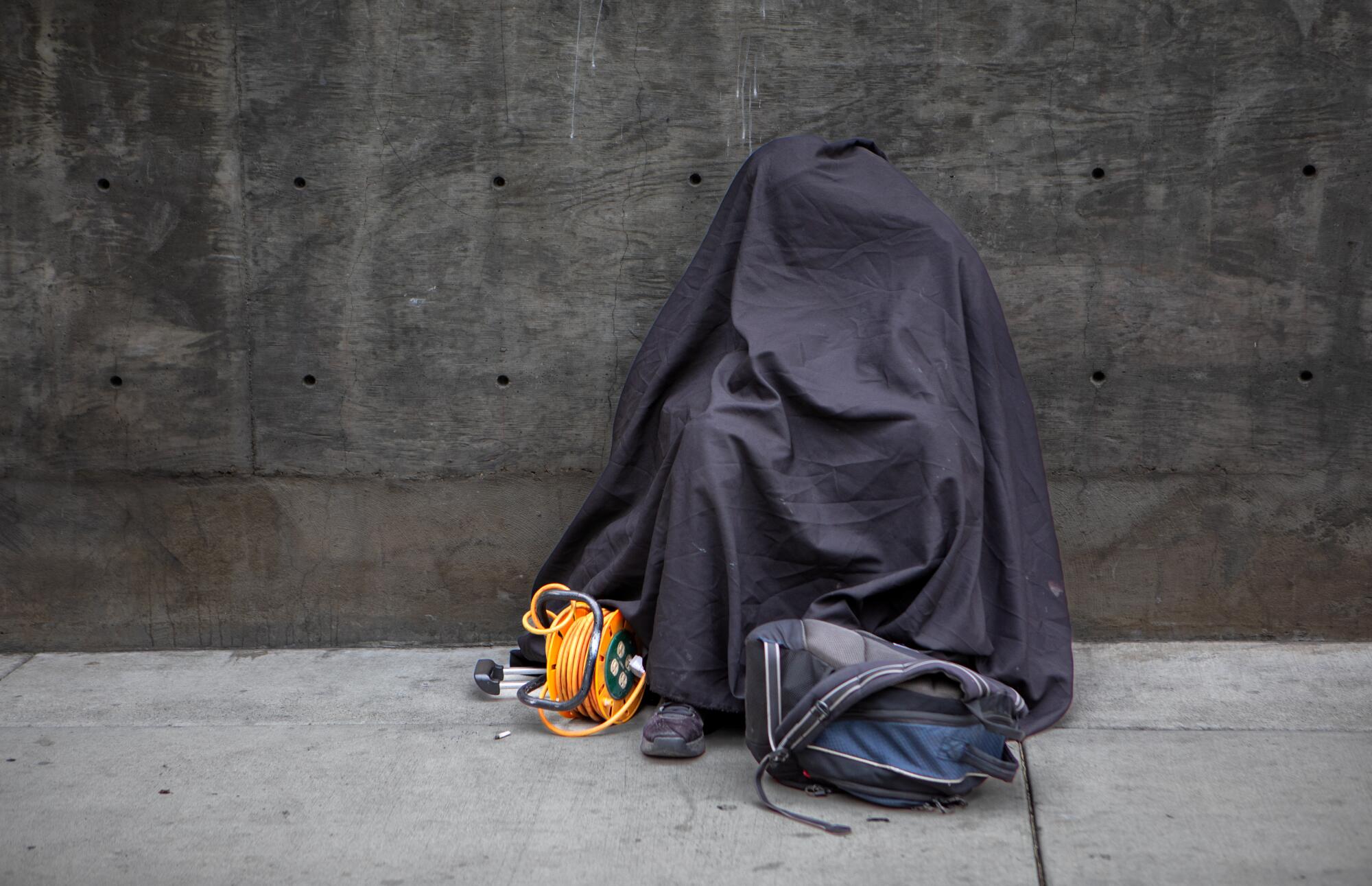 A personcovered in cloth sits on a sidewalk.