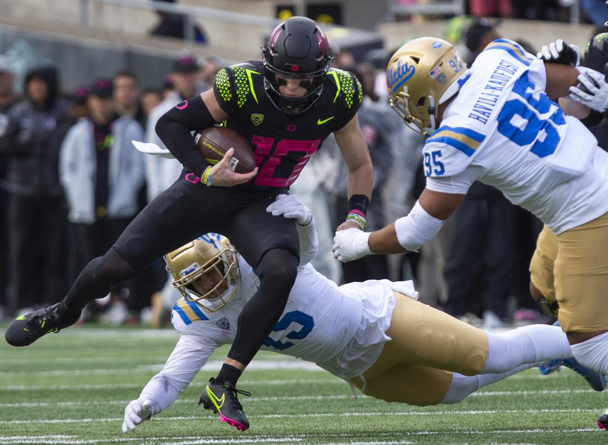 Oregon quarterback Bo Nix, left, carries the ball against UCLA's Laiatu Latu, bottom, and Sitiveni Havili-Kaufusi