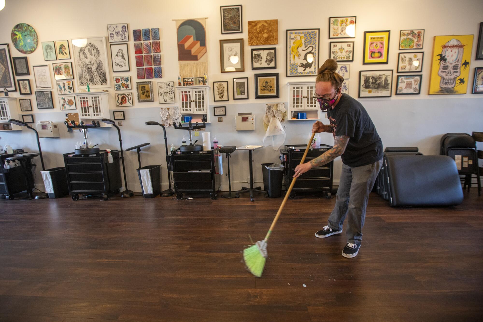 A man wearing a mask sweeps the floor of a business