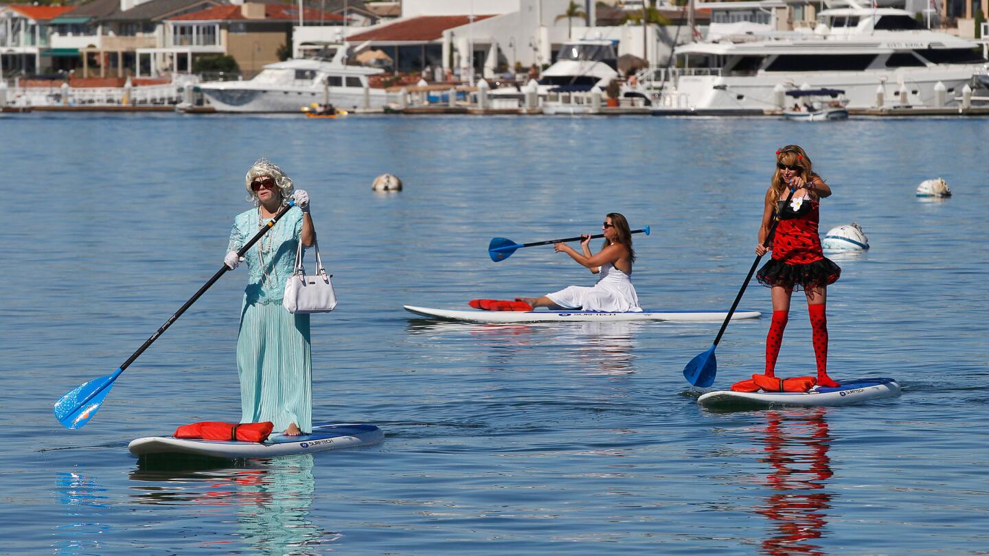 Debby Falese of Huntington Beach, dressed as Queen Elizabeth, left; Jennifer Calonico of Laguna Beach, dressed as Marilyn Monroe; and Courtney Knapp of San Clemente, dressed as a ladybug, paddle through Newport Harbor on Halloween.