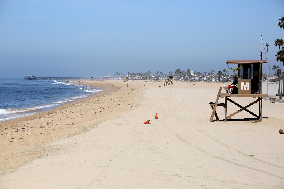 A lifeguard keeps an eye on a mostly empty beach next to the Balboa Pier in Newport Beach.
