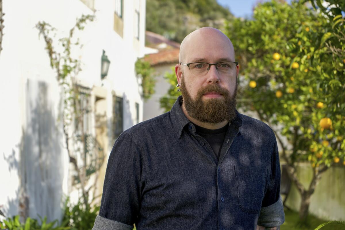 A man with a beard wears a dark shirt and glasses.