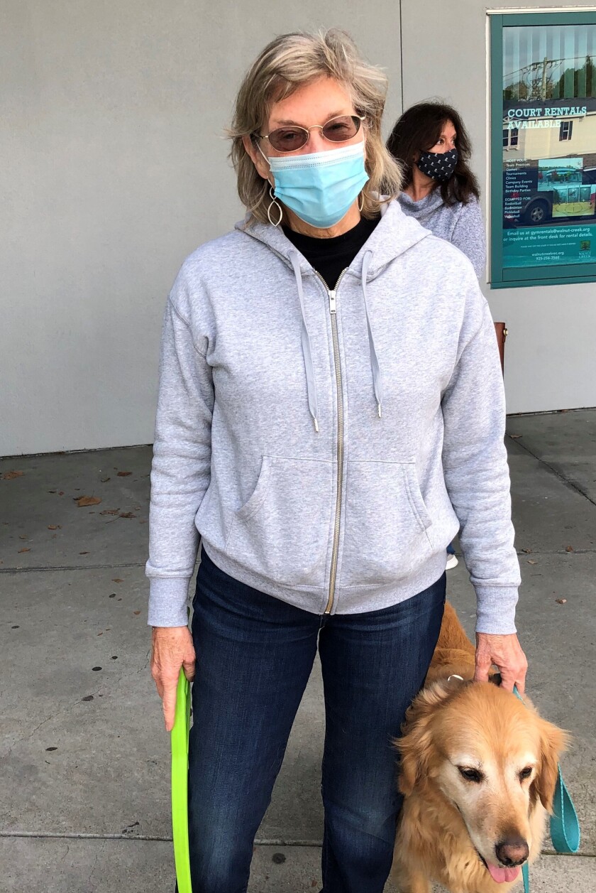 A woman in a mask stands with her golden retriever.