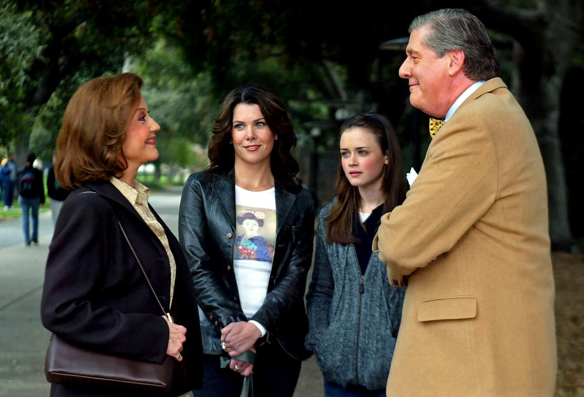 A woman and her daughter stand outside looking at their parents smiling at each other. 