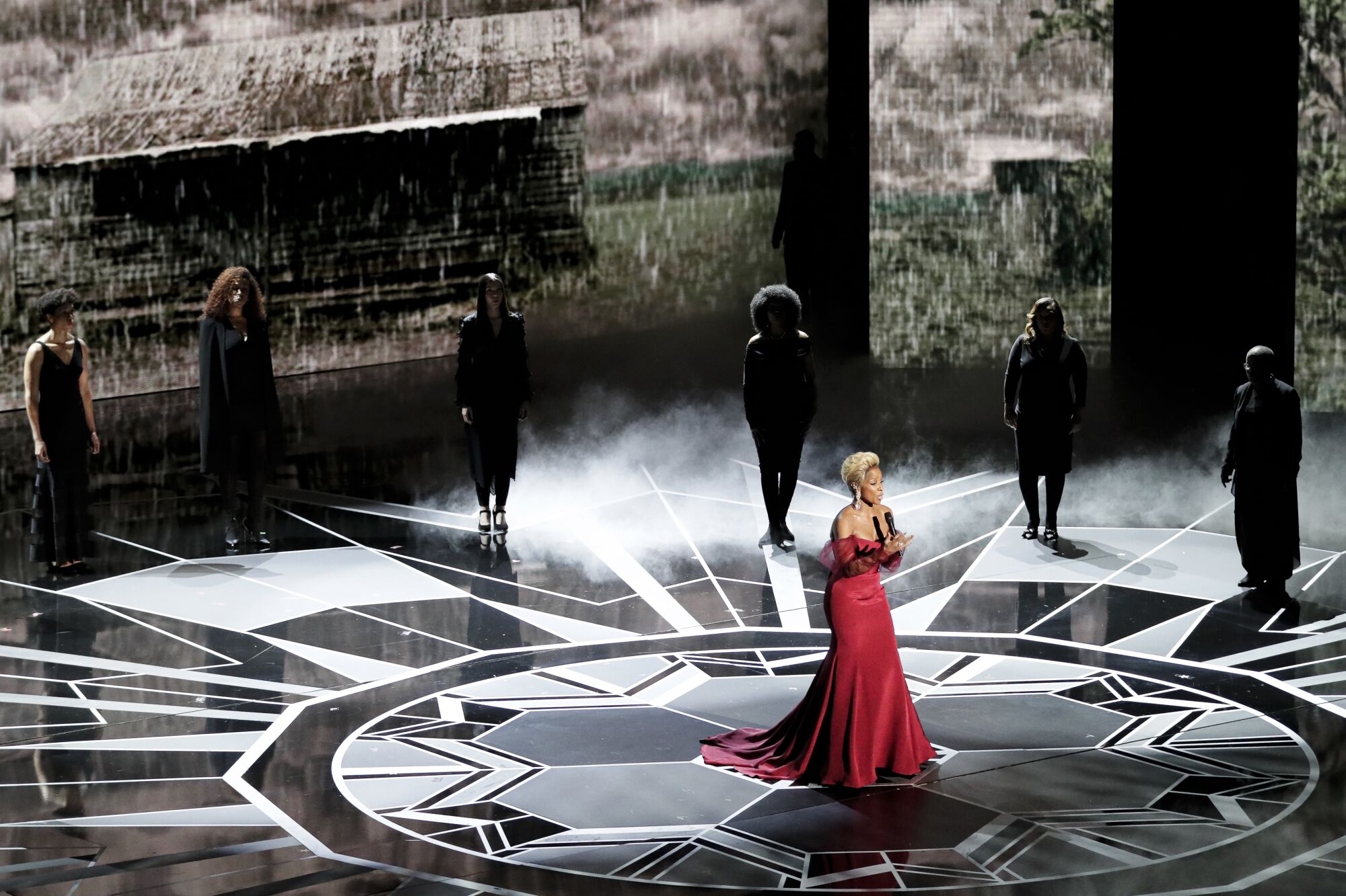 A woman in a red dress performs on a stage under lights.