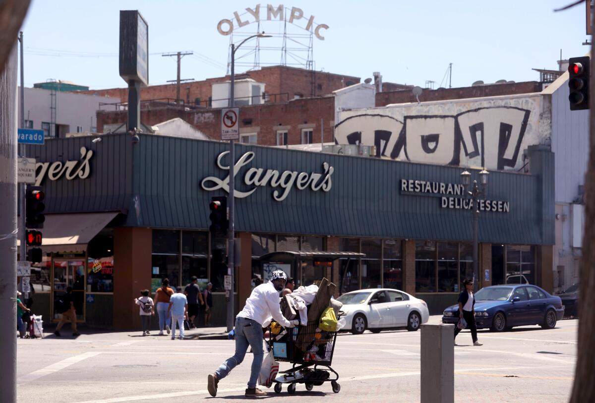 A man walks with his belongings in a shopping cart across from Langer's deli.