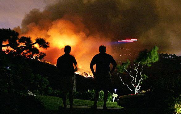 Residents of Cartier Drive in Rancho Palos Verdes watch as a helicopter, right, makes a water run at a brush fire in the Portuguese Bend area.