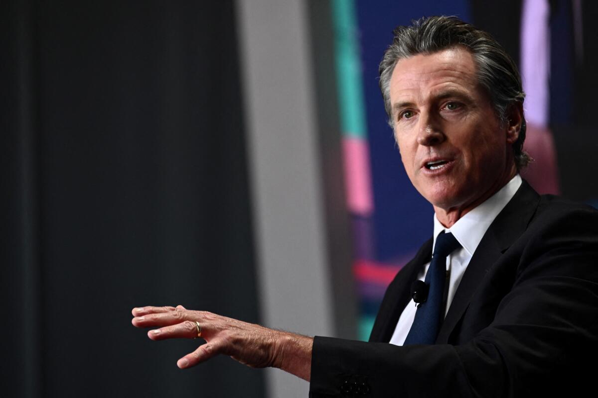 A man in dark suit and tie gestures with one hand while speaking 