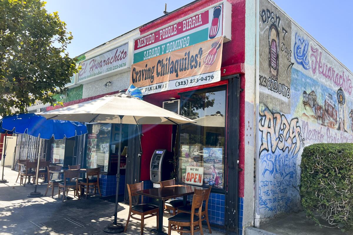 Tables and chairs sit under umbrellas outside a small storefront.