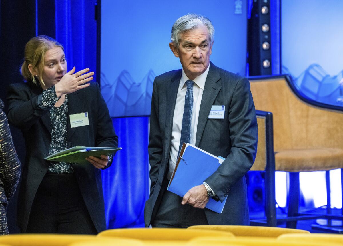 Jerome Powell stands at a symposium holding a folder.