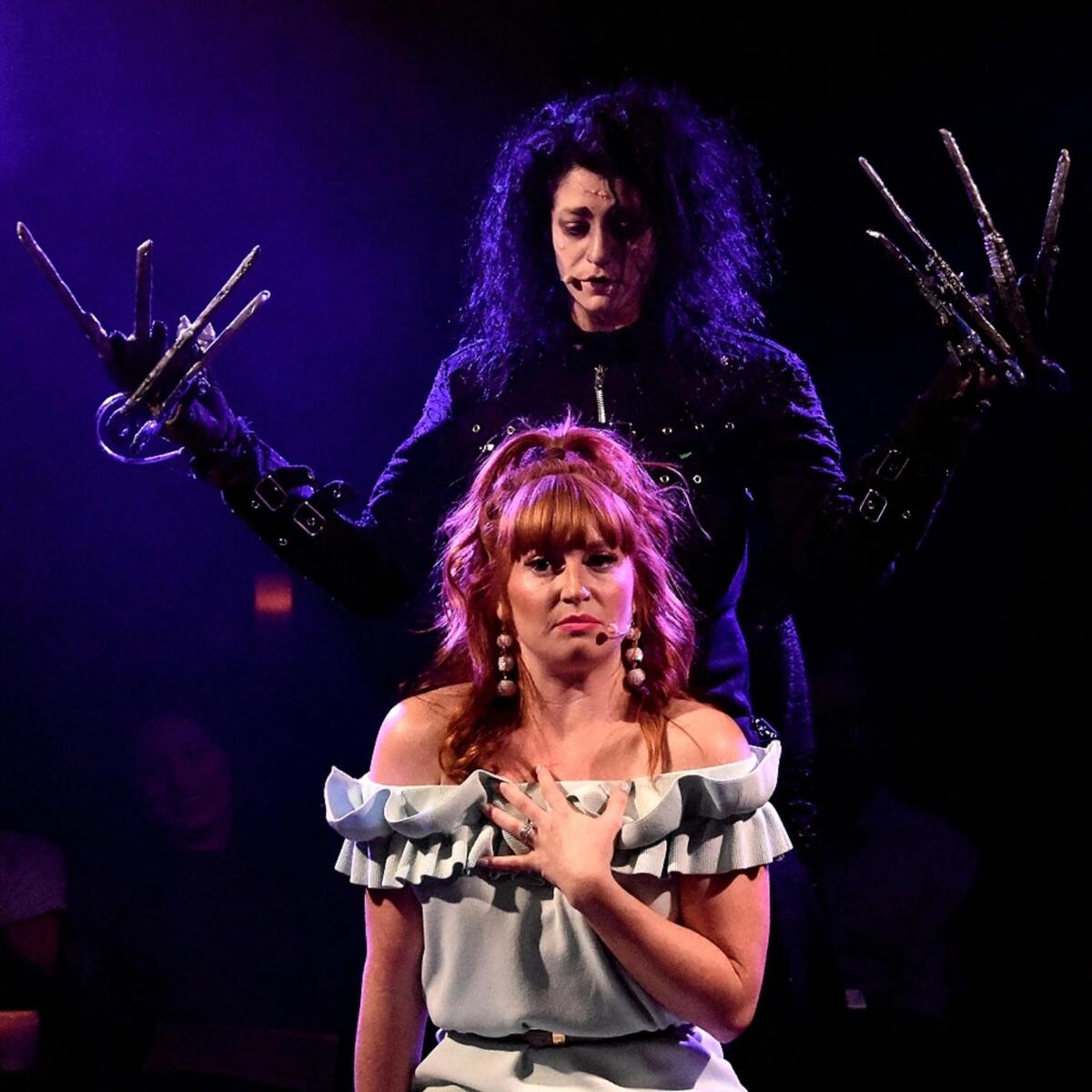 A woman on her knees looking forward while Scissorhands steps behind her.