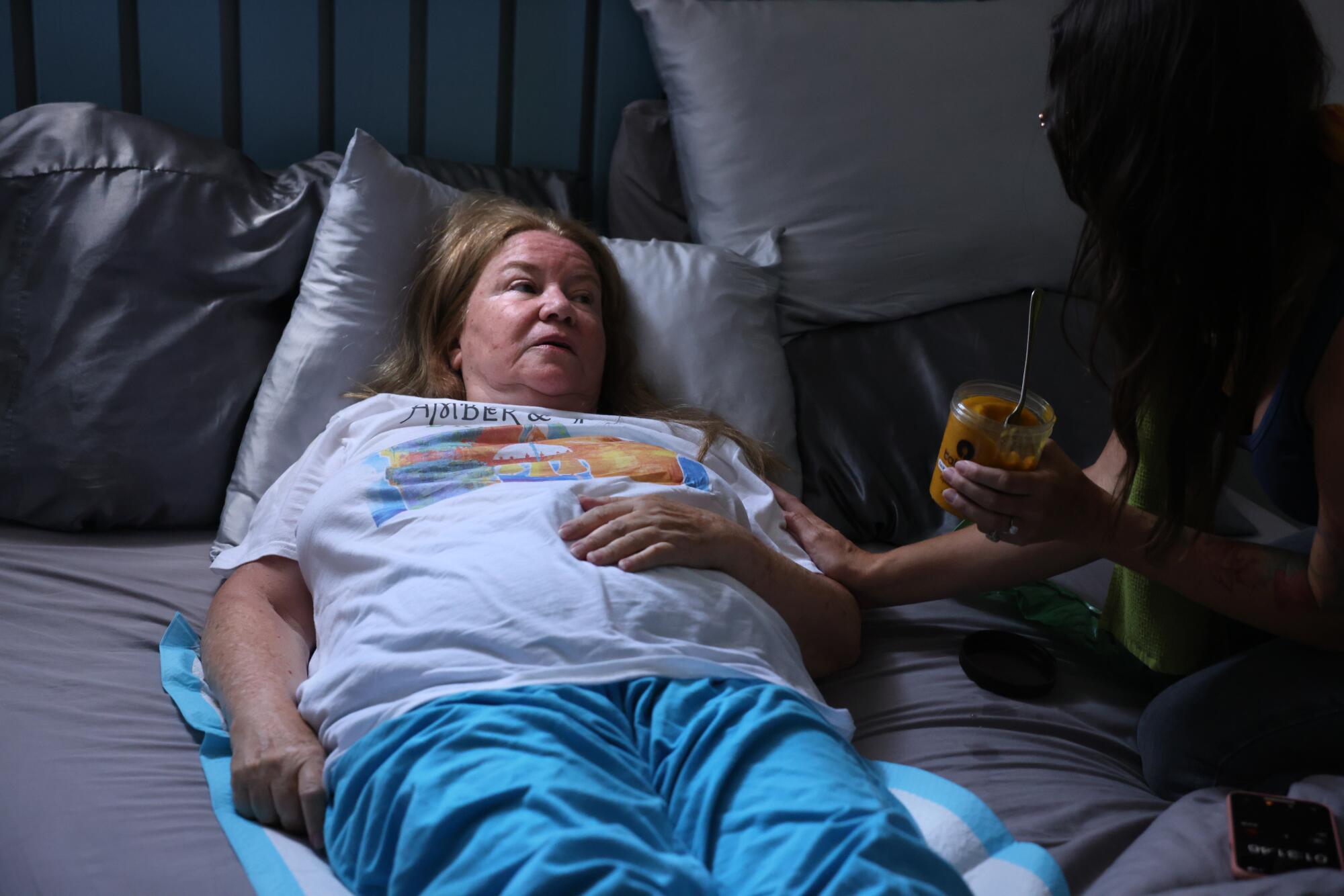 A woman rests on bed next to another woman