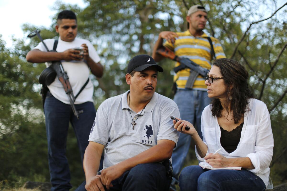 Katherine Corcoran interviews a man using a tape recorder while men carrying automatic weapons watch.