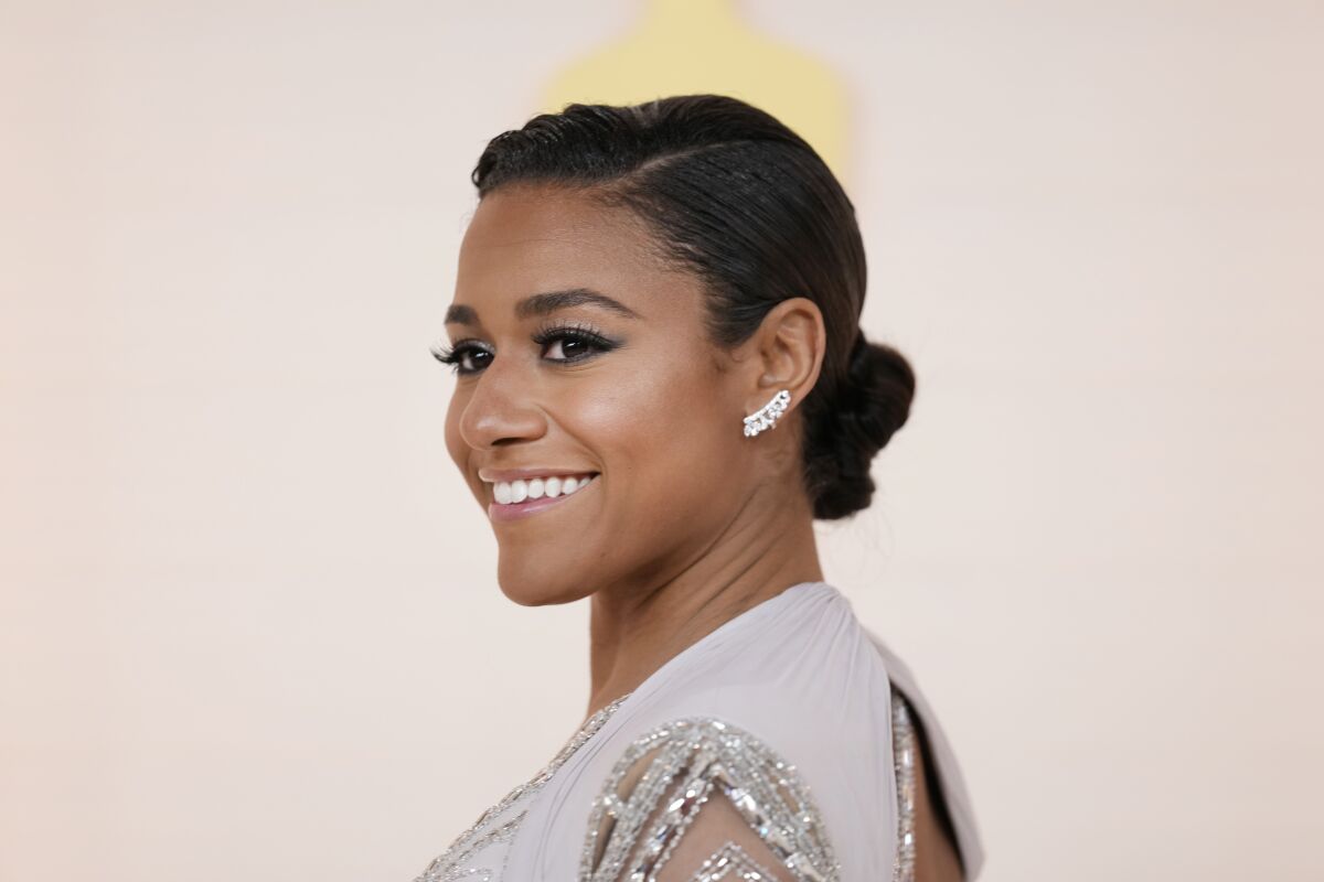 Ariana DeBose smiles in a sparkly dress against a cream background.