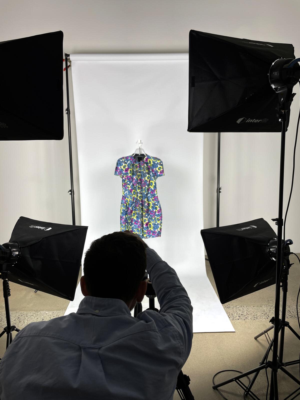 A dress hung against a blank backdrop is photographed.