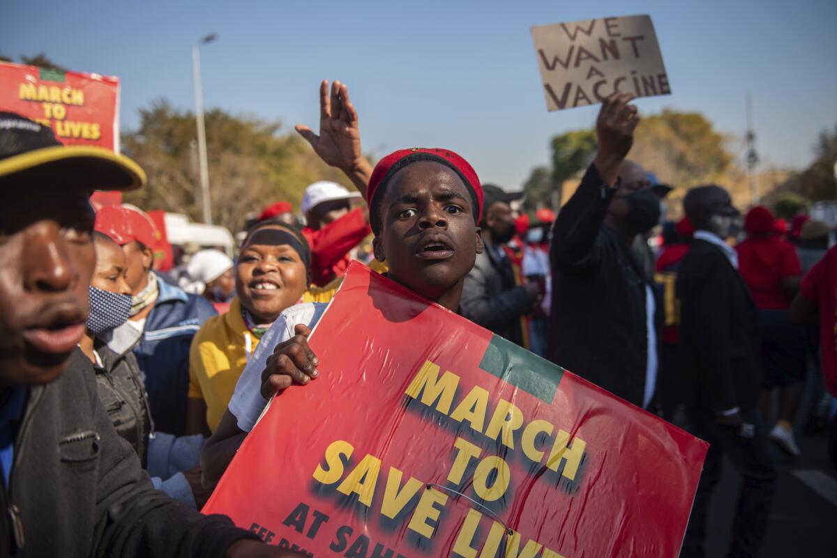 A crowd of people hold signs including "March to Save Lives" and "We Want a Vaccine."