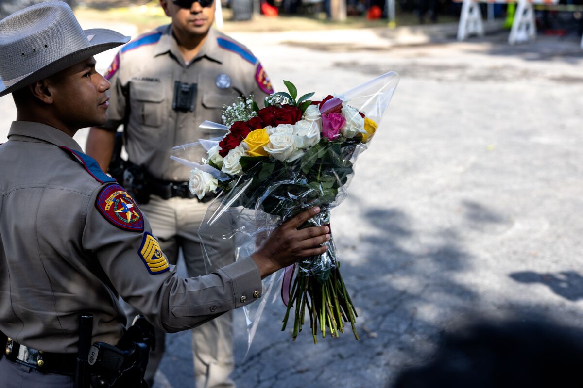 A Texas State Trooper receives flowers for the victims of a mass shooting yesterday at Robb Elementary School 