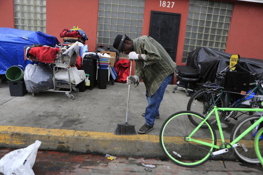 A homeless man tidies up the spot where his belongings are gathered on South Hope Street in Los Angeles.