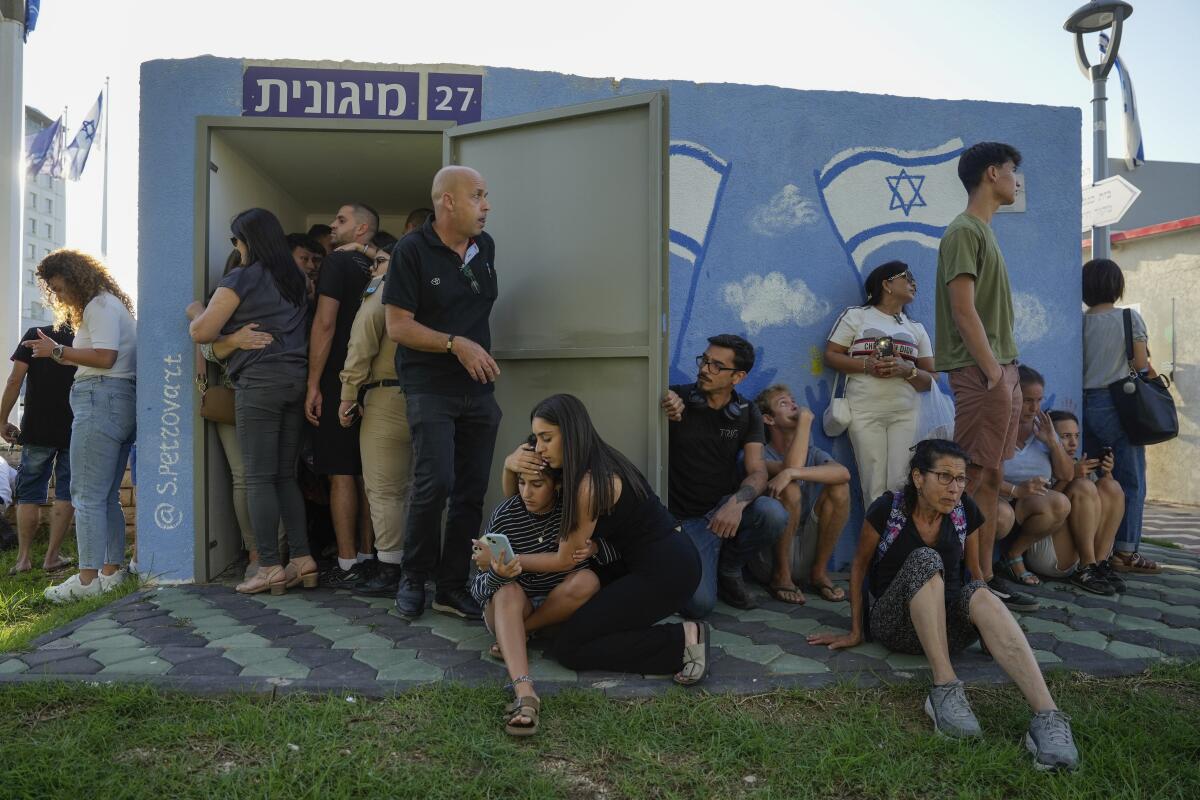 Israelis take cover next to a shelter as a siren sounds a warning of incoming rockets fired from Lebanon, in 