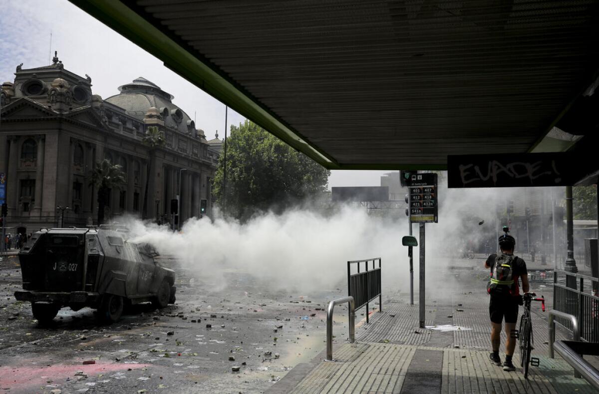 Un hombre camina con su bicicleta mientras un vehículo policial rocía gases lacrimógenos durante una protesta en Santiago, Chile, el miércoles 23 de octubre de 2019. Un día después de anunciar medidas para mitigar la crisis social más grave en 30 años de democracia, el gobierno del presidente chileno Sebastián Piñera no lograba contener el miércoles los disturbios, que han dejado un saldo de al menos 18 muertos. (AP Foto/Rodrigo Abd)