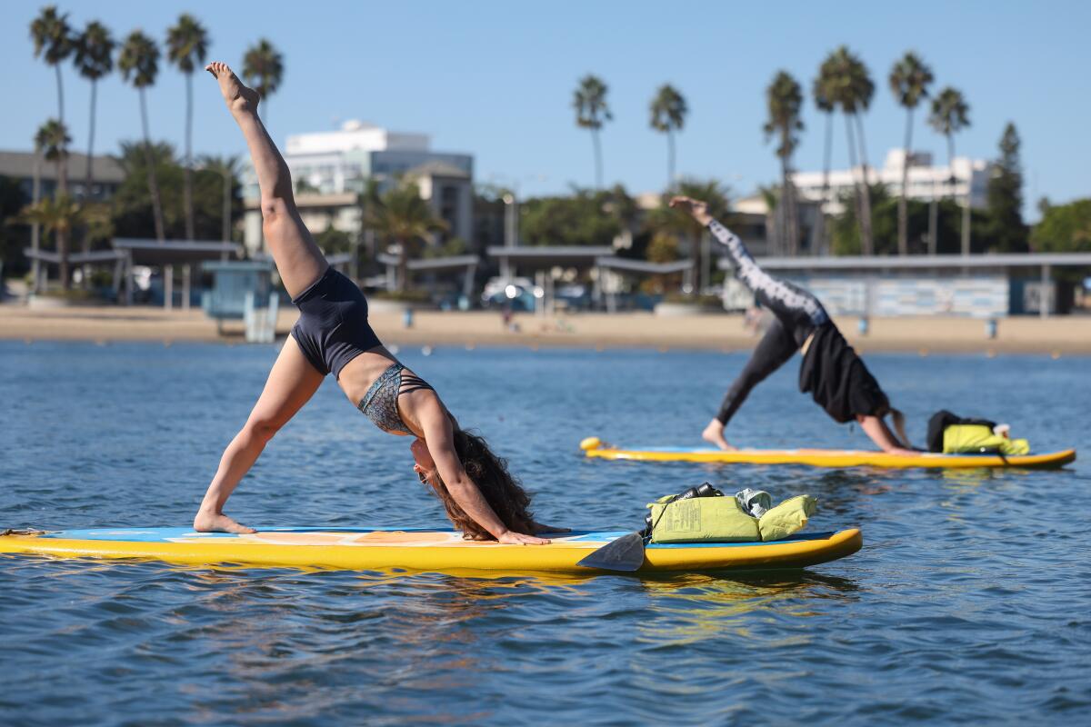 Two people do yoga poses on surfboards on the water