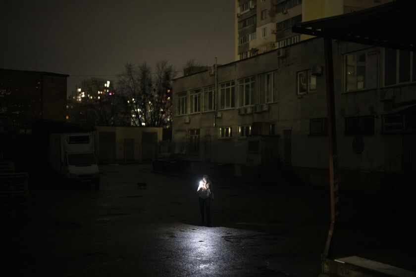 A woman uses her phone to light her way in Kyiv, Ukraine, Tuesday, Jan. 31, 2023. (AP Photo/Daniel Cole)