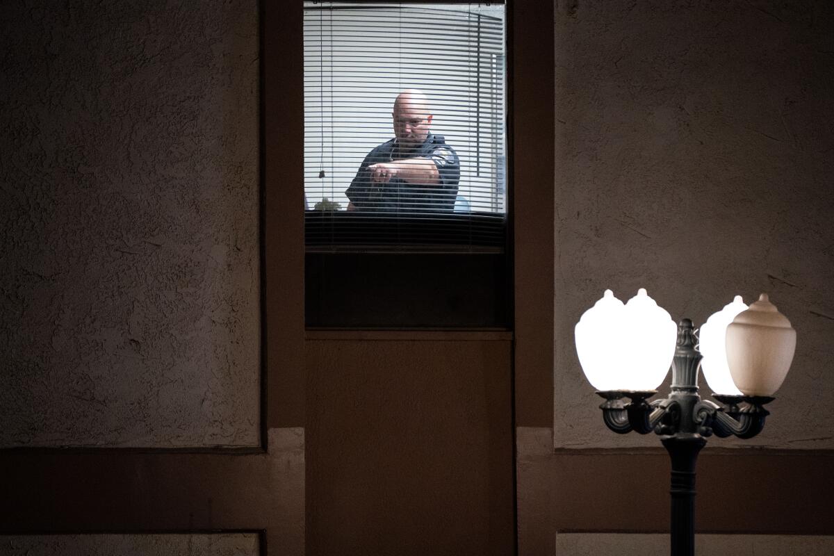 A police officer seen through a window at night points at something in a room