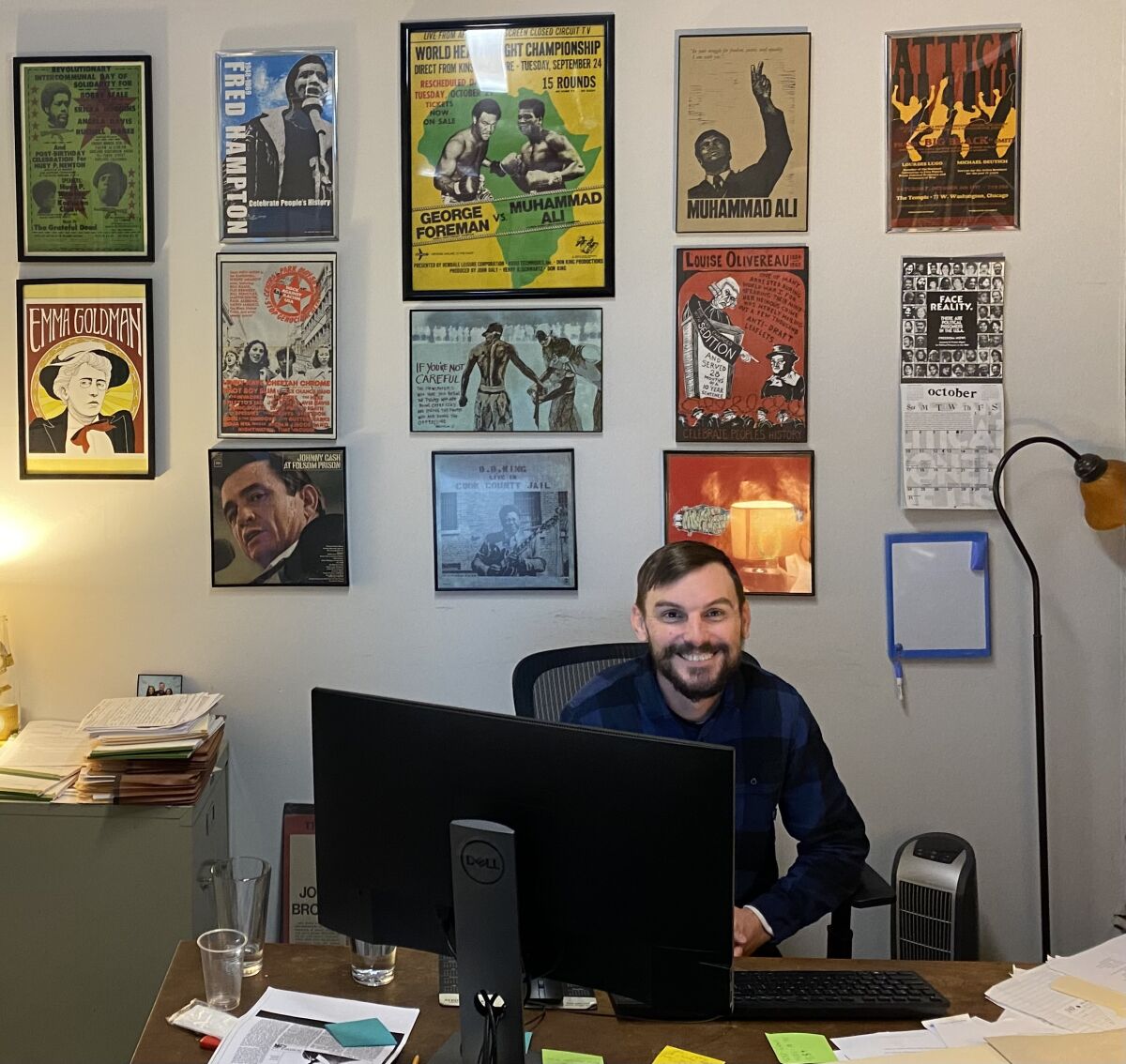 Brad Thomson sitting behind a desk in an office decorated with posters of pop culture and political heroes.