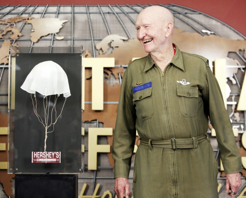 Gail Halvorsen in uniform stands next to a parachute and candy bar.