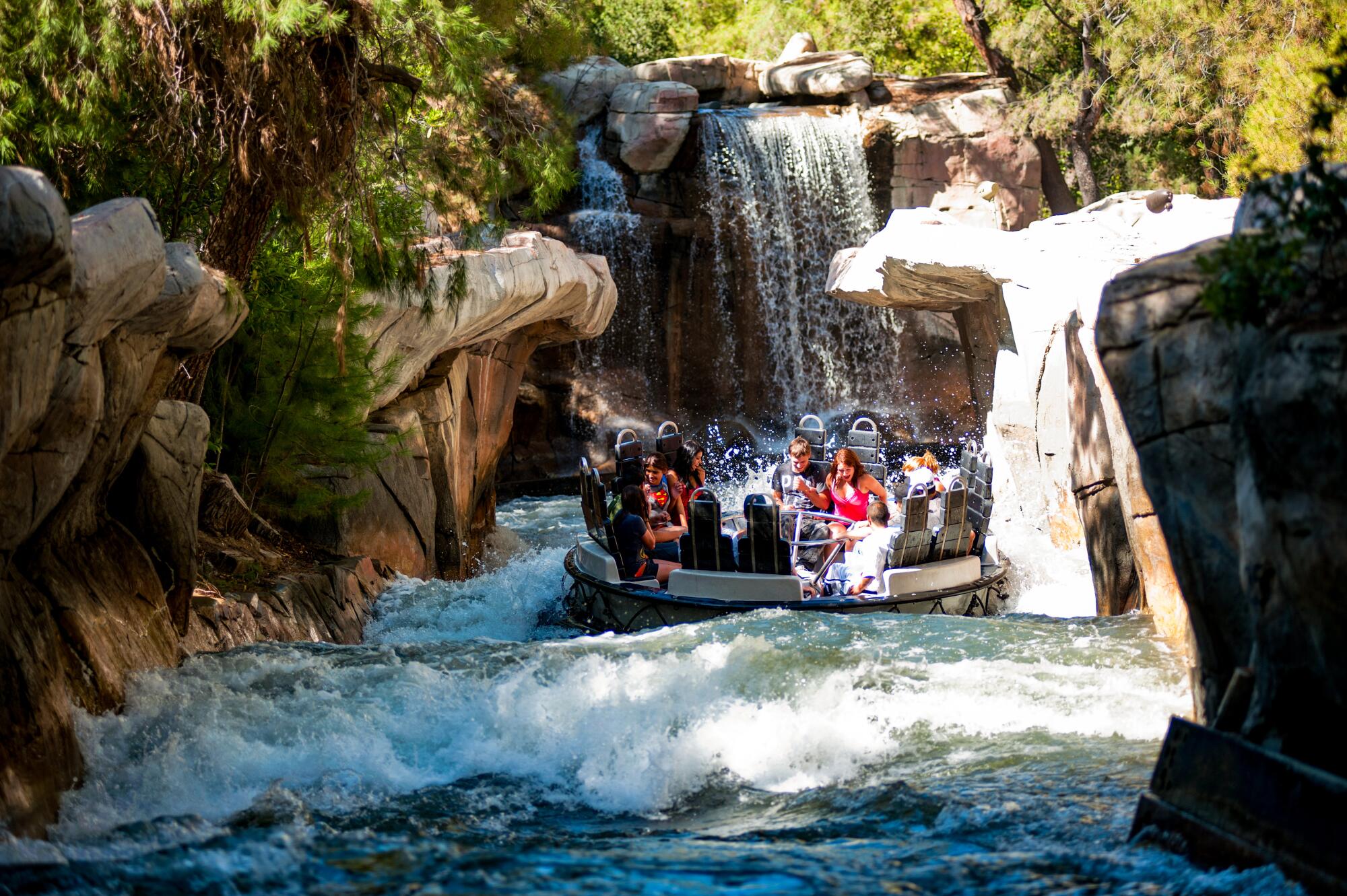 A boat full of people floats in a rocky channel amid rapids at a theme park