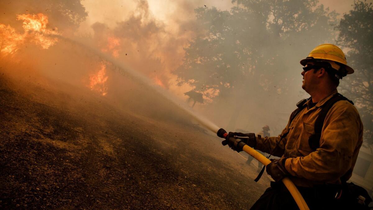 Firefighters work to keep flames from the River fire from reaching a home as evening winds kick up near Lakeport, Calif., on July 31.