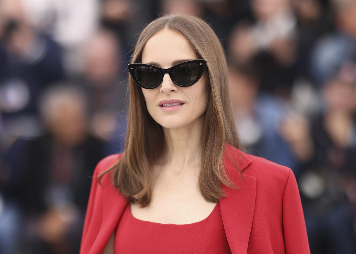 Natalie Portman wears black cat-eye sunglasses and a red blazer over her shoulders and red top