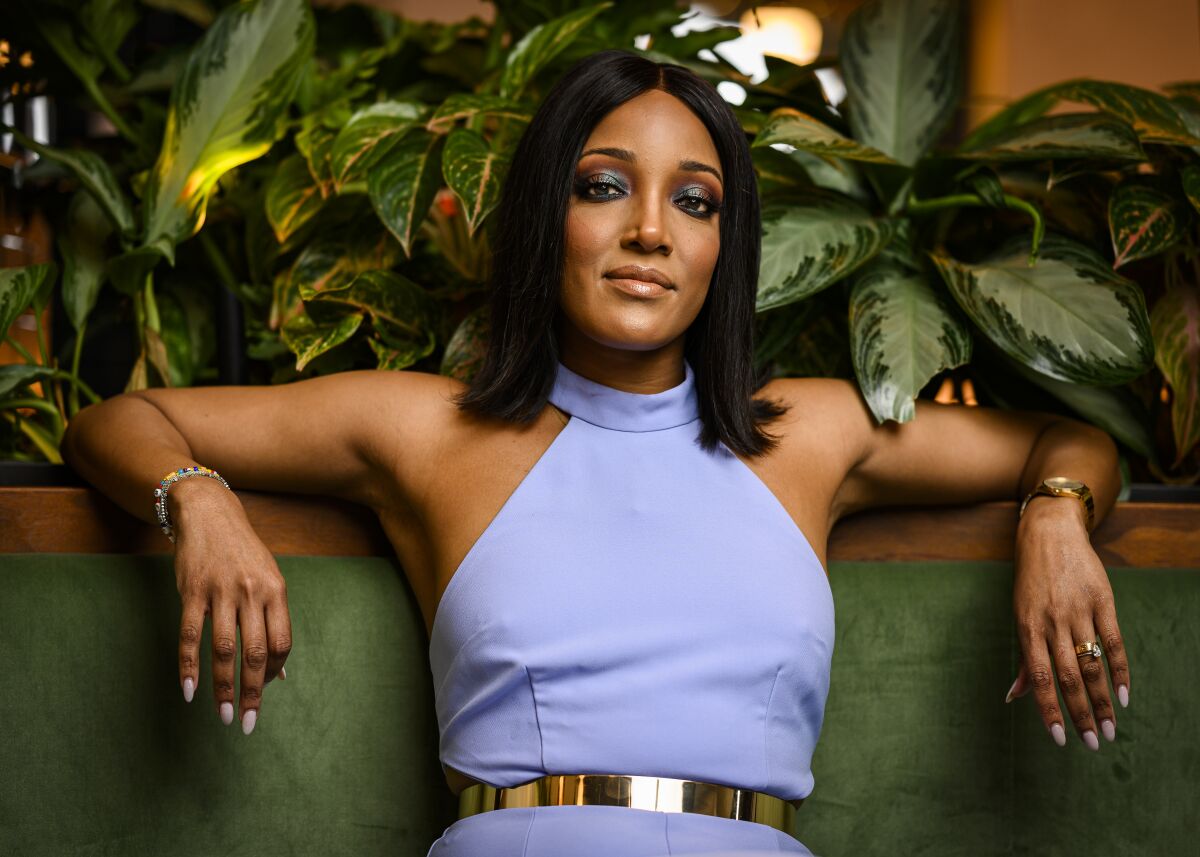 Singer Mickey Guyton lounges on a green chair in a lavender halter dress