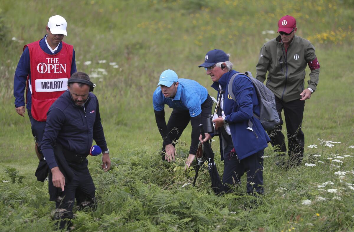 Rory McIlroy has help looking for his ball after hitting into the long rough near the green on the first hole.