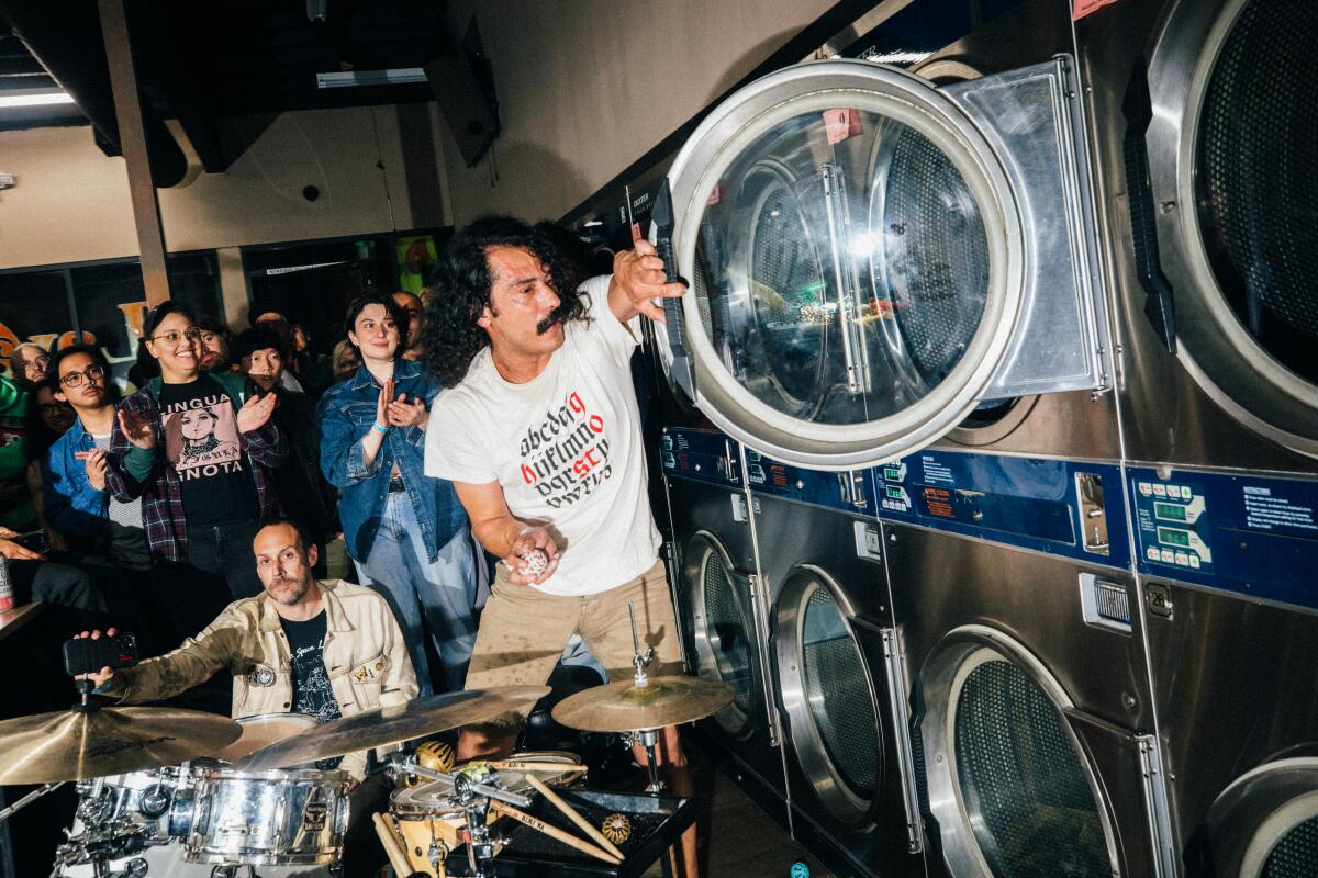 A drummer stands and opens the door of a large dryer inside a laundromat.