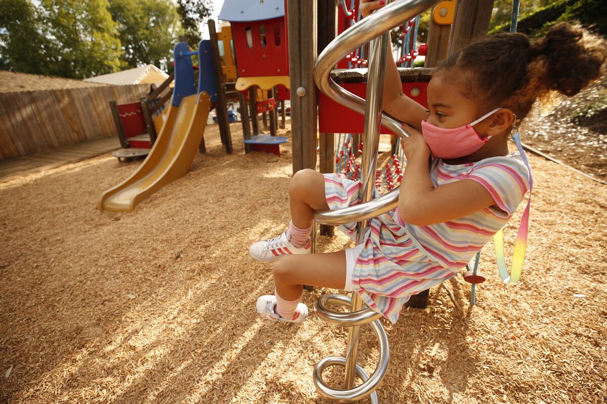 A kindergartener wears a face mask while on playground equipment