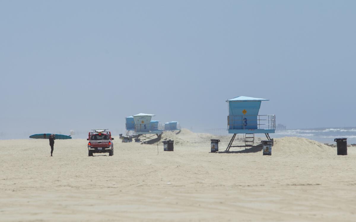 A Huntington Beach lifeguard speaks with a surfer on a nearly deserted stretch of the beach south of the Huntington Beach Pier on Tuesday.