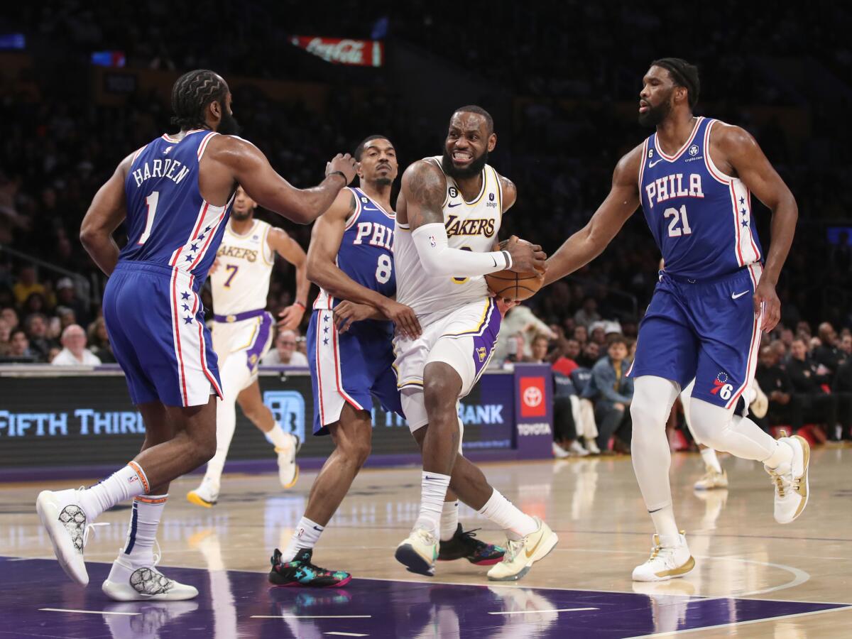 Lakers star LeBron James drives to the basket between 76ers guard James Harden and center Joel Embiid.